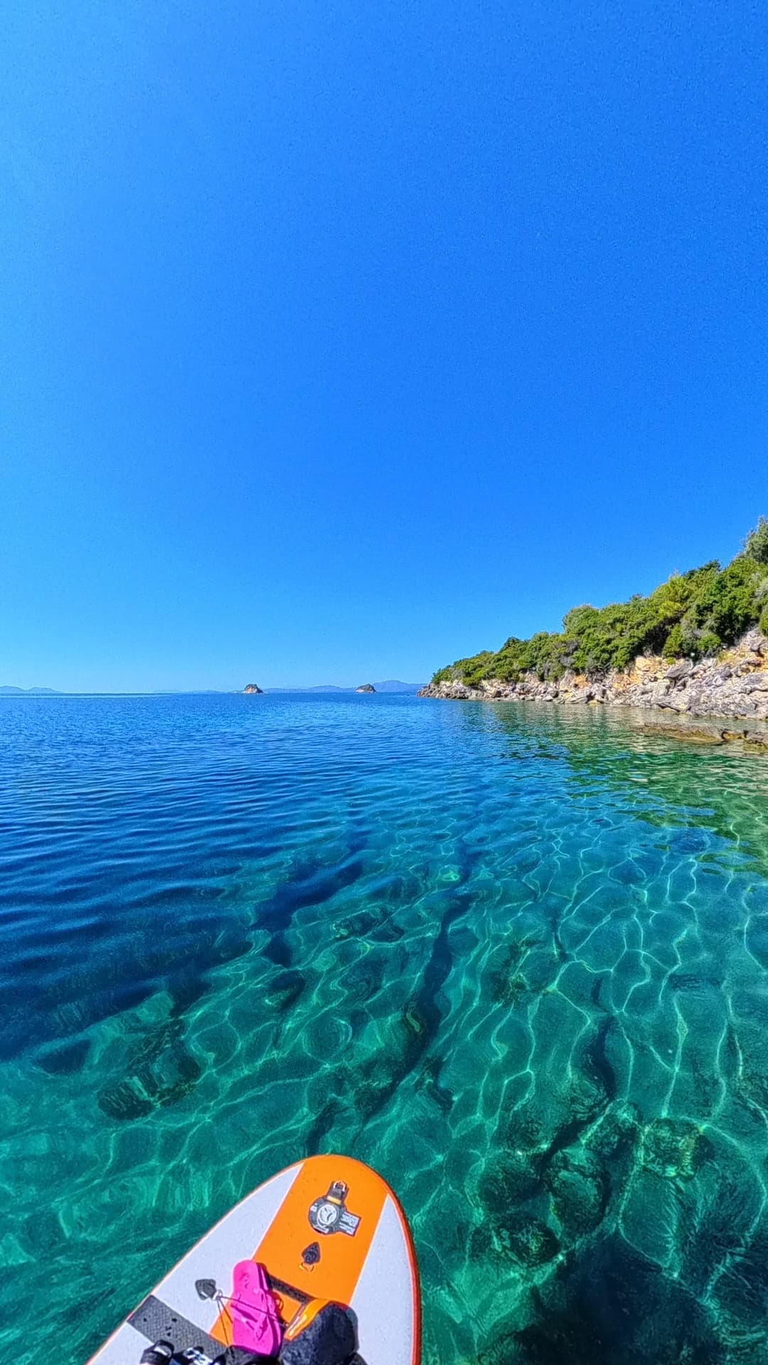 View from a paddleboard over crystal clear water towards distant islands