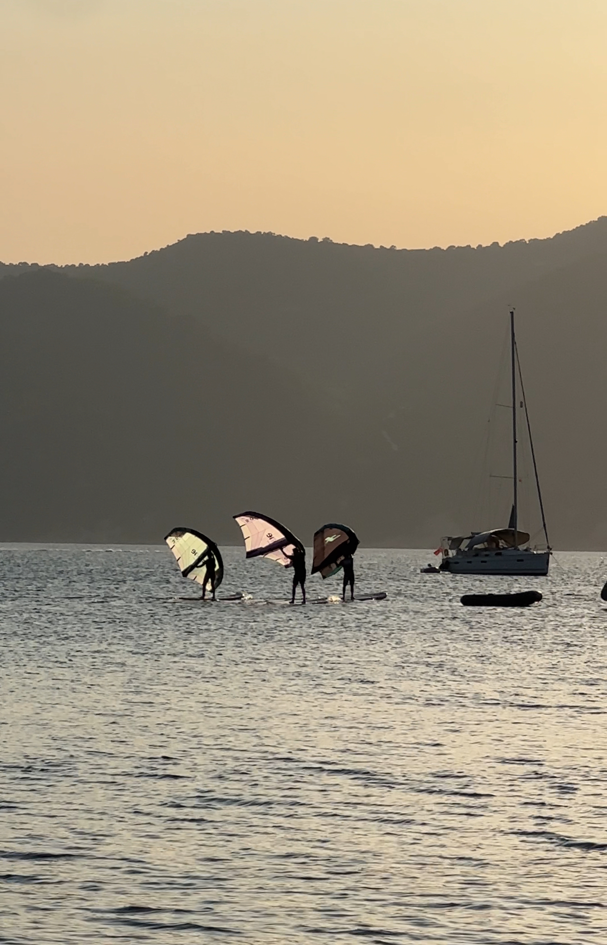 Three wing surfers / wing foilers riding at sunset on the Ionian Sea