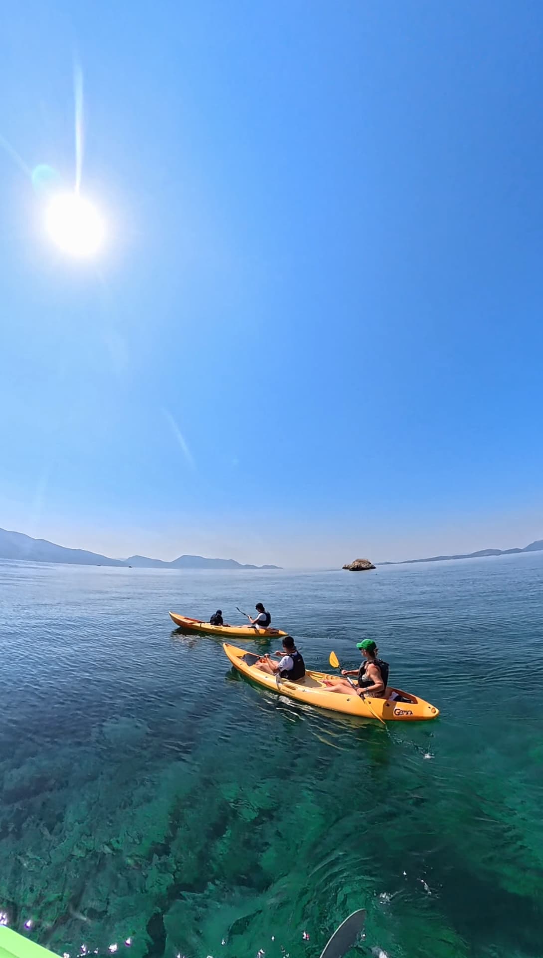 Two kayaks paddling on calm sunlit Ionian water near a small island