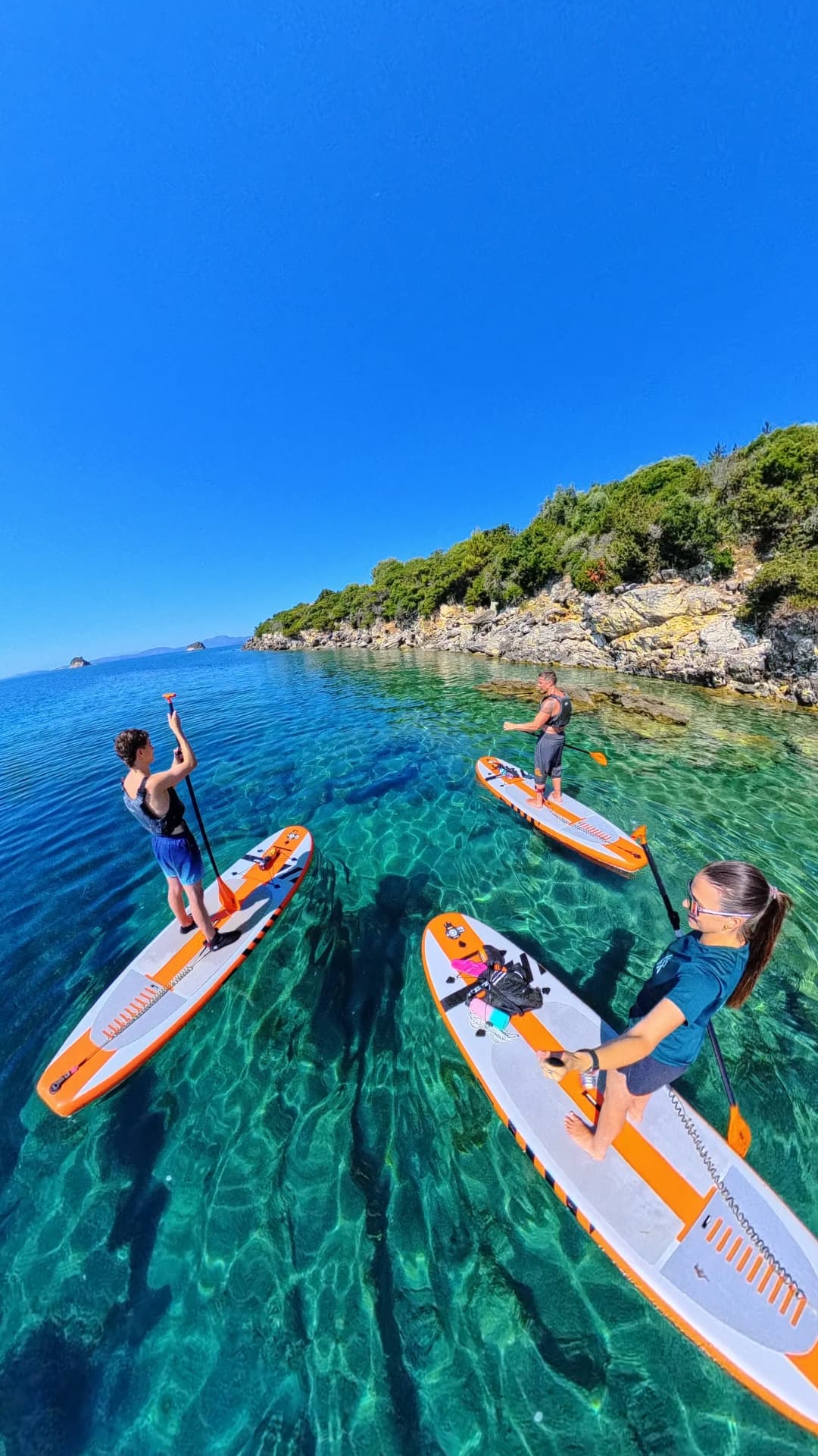 Group of paddleboarders exploring a rocky cove on clear Ionian water