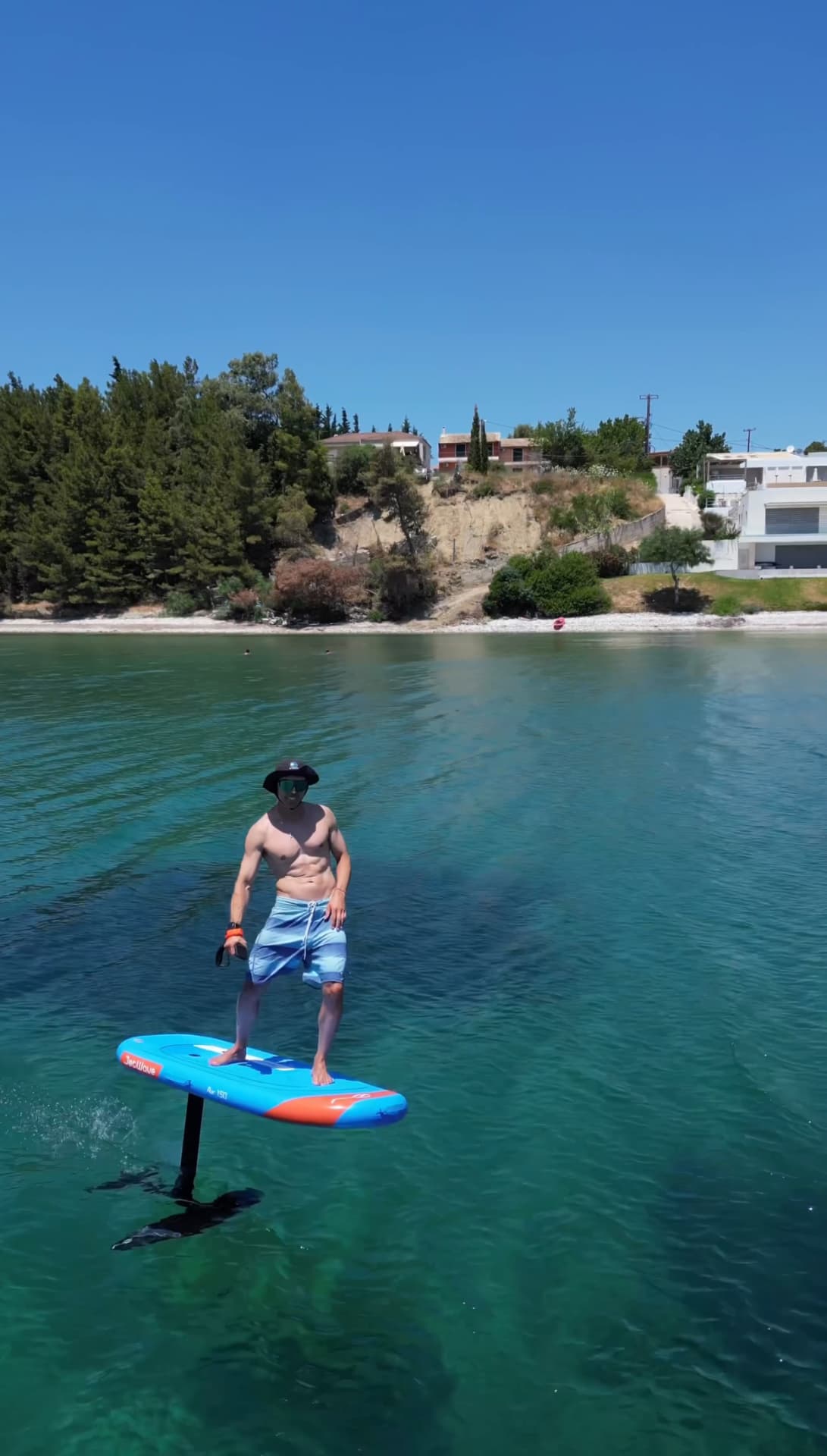 E-foil rider gliding across a quiet bay in front of pine trees and houses